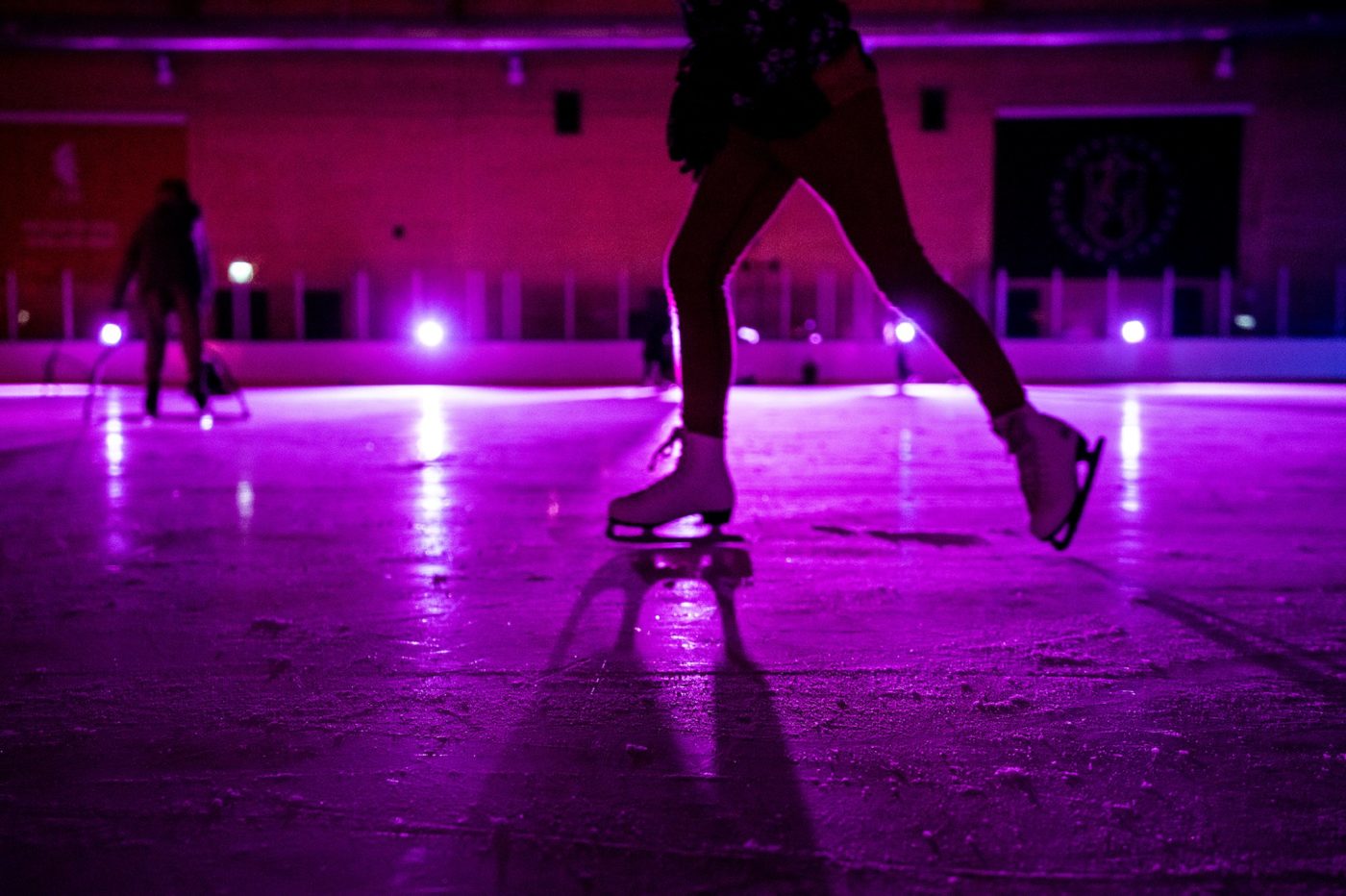 Is som är upplyst med lila discoljus. På isen ser man siluetter av två karaktärer som åker skridskor. 