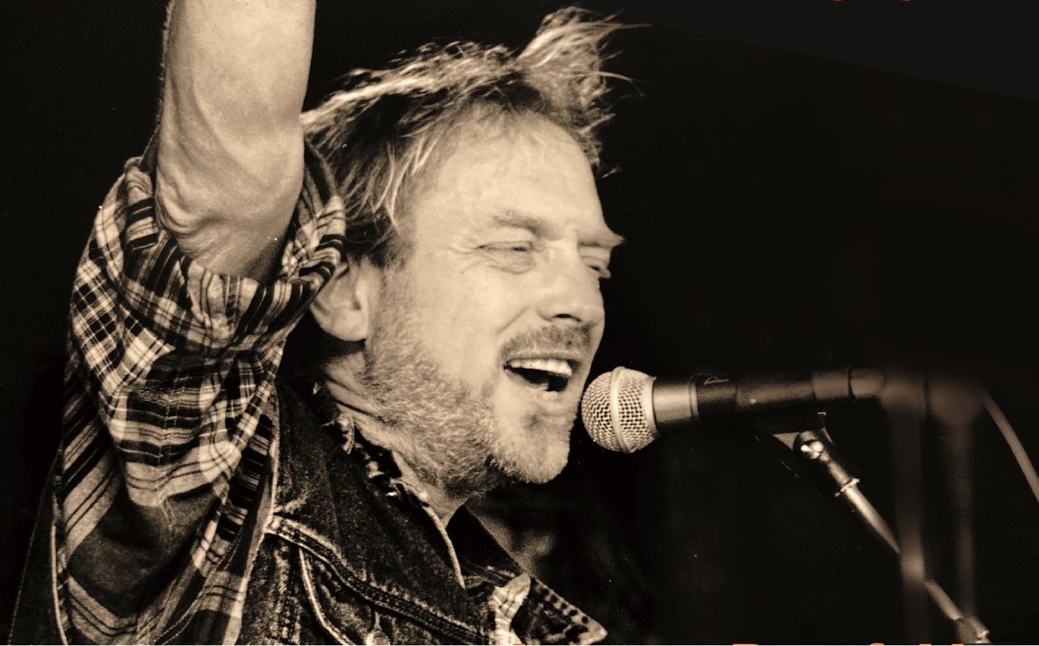 Man i rutig skjorta sjunger i en mikrofon och har ena armen upplyft. Orange text med titeln Rainrock Hyllning till Pugh