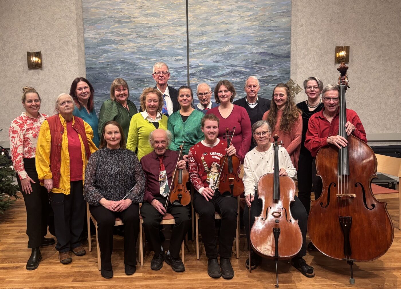En orkester är samlad för ett gruppfoto framför en blå stor målning. Några av musikerna håller i sina stråkinstrument.
