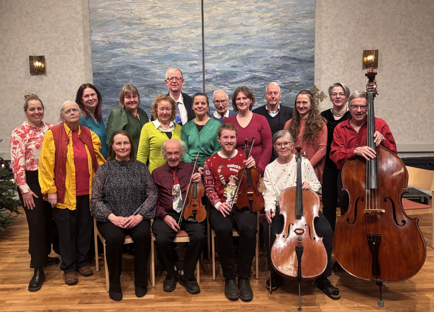En orkester är samlad för ett gruppfoto framför en blå stor målning. Några av musikerna håller i sina stråkinstrument.