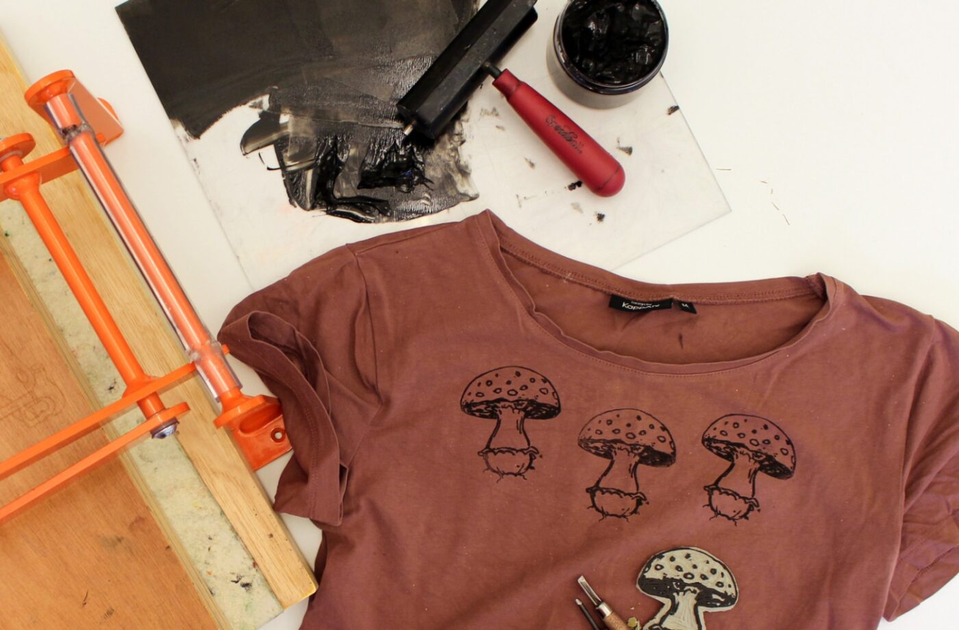 brun t-shirt med svamptryck och tryckverktyg på en vit bordsskiva